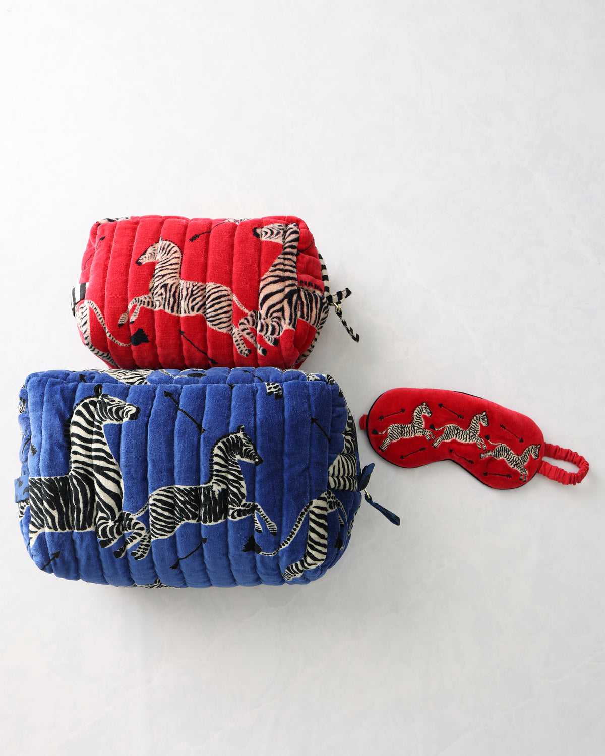 Zebra-print bundle with red and blue quilted pouches and a red eye mask.