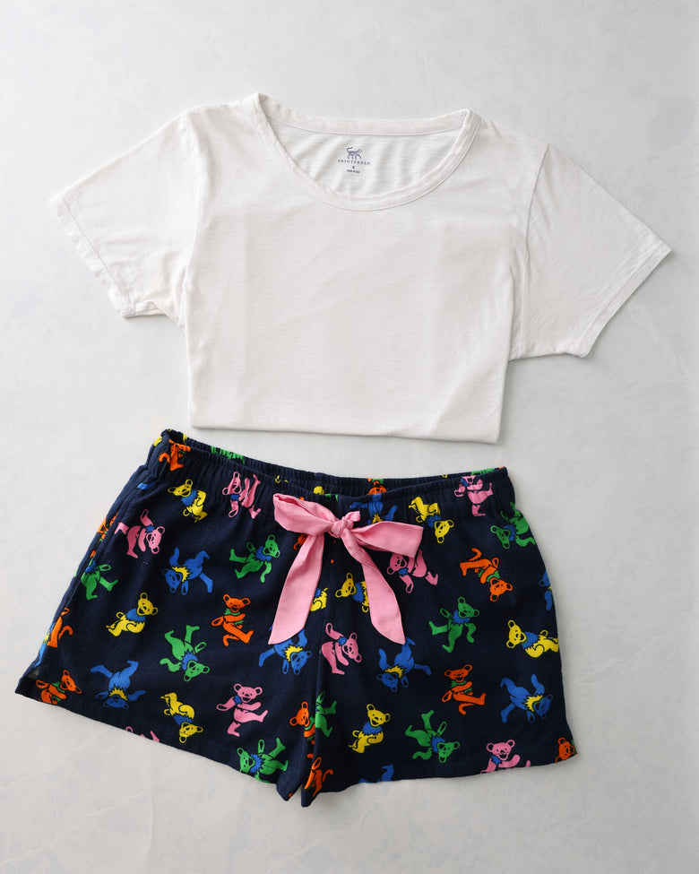 Flat lay of a white short-sleeve tee and navy pajama shorts with colorful dancing bear figures and a pink waist tie.
