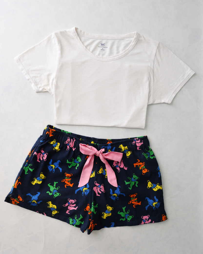 Flat lay of a white short-sleeve tee and navy pajama shorts with colorful dancing bear figures and a pink waist tie.