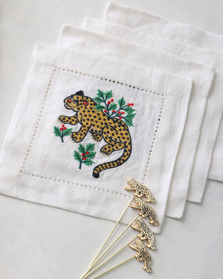 Close-up of an embroidered leopard cocktail napkin with four leopard-shaped cocktail picks.