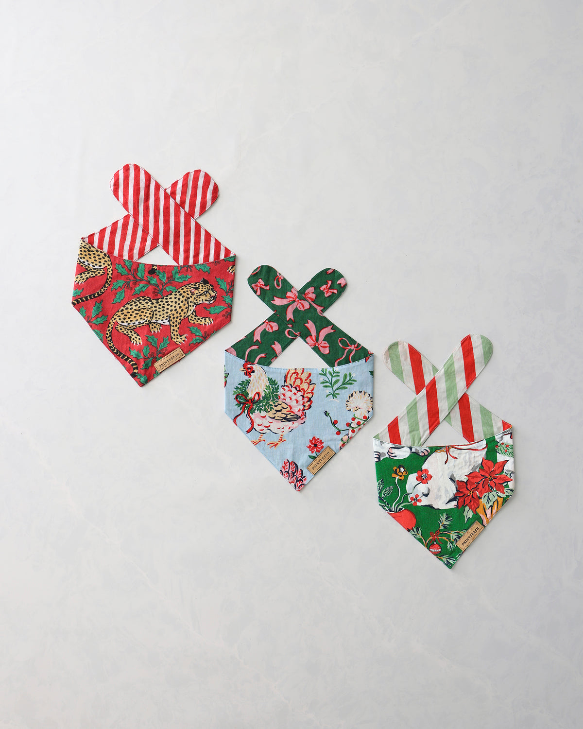 Three pet bandanas with holiday prints, including leopard, floral, and dog designs.