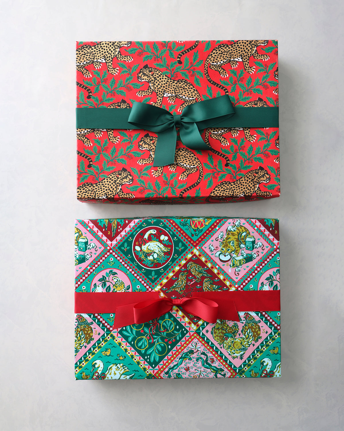 Two rectangular handmade gift boxes shown front-on: one with a red leopard-and-holly print and green ribbon, and one with a multicolored holiday print and red ribbon.