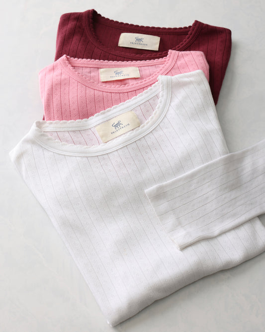 Three folded pointelle long-sleeve shirts in burgundy, pink, and white.