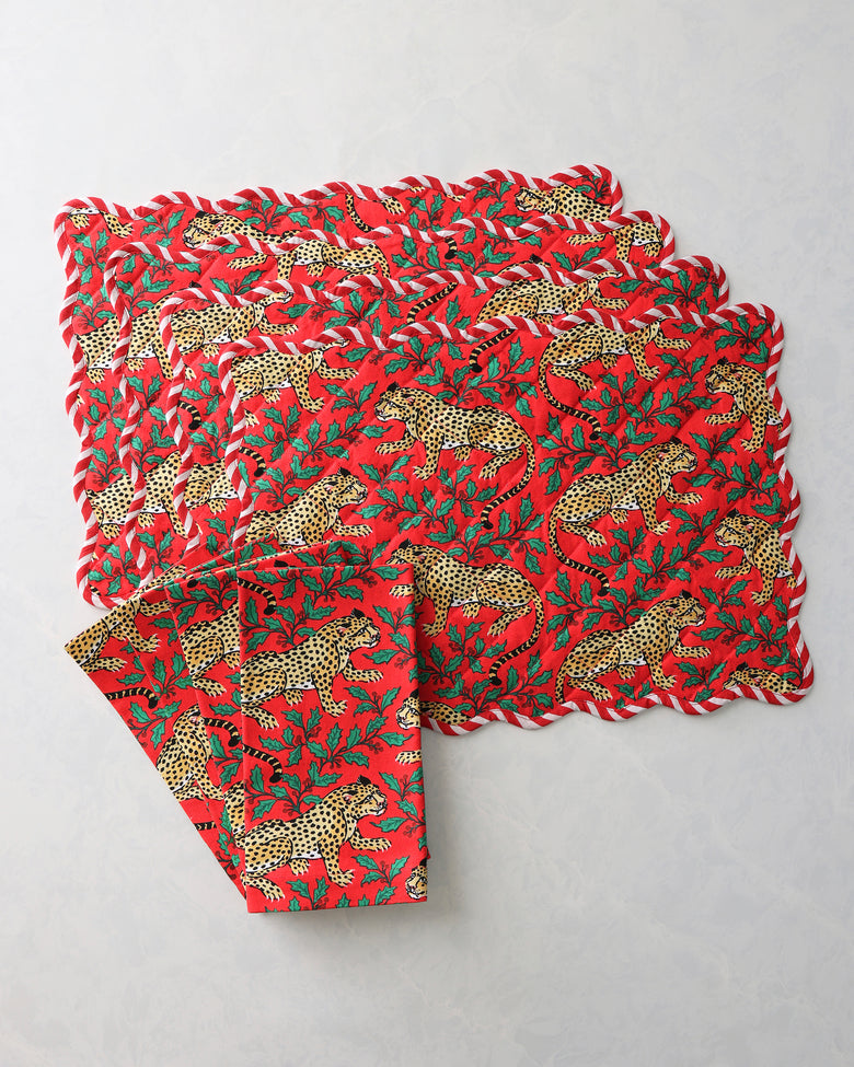 Stacked red placemats and napkins with leopard and holly print.