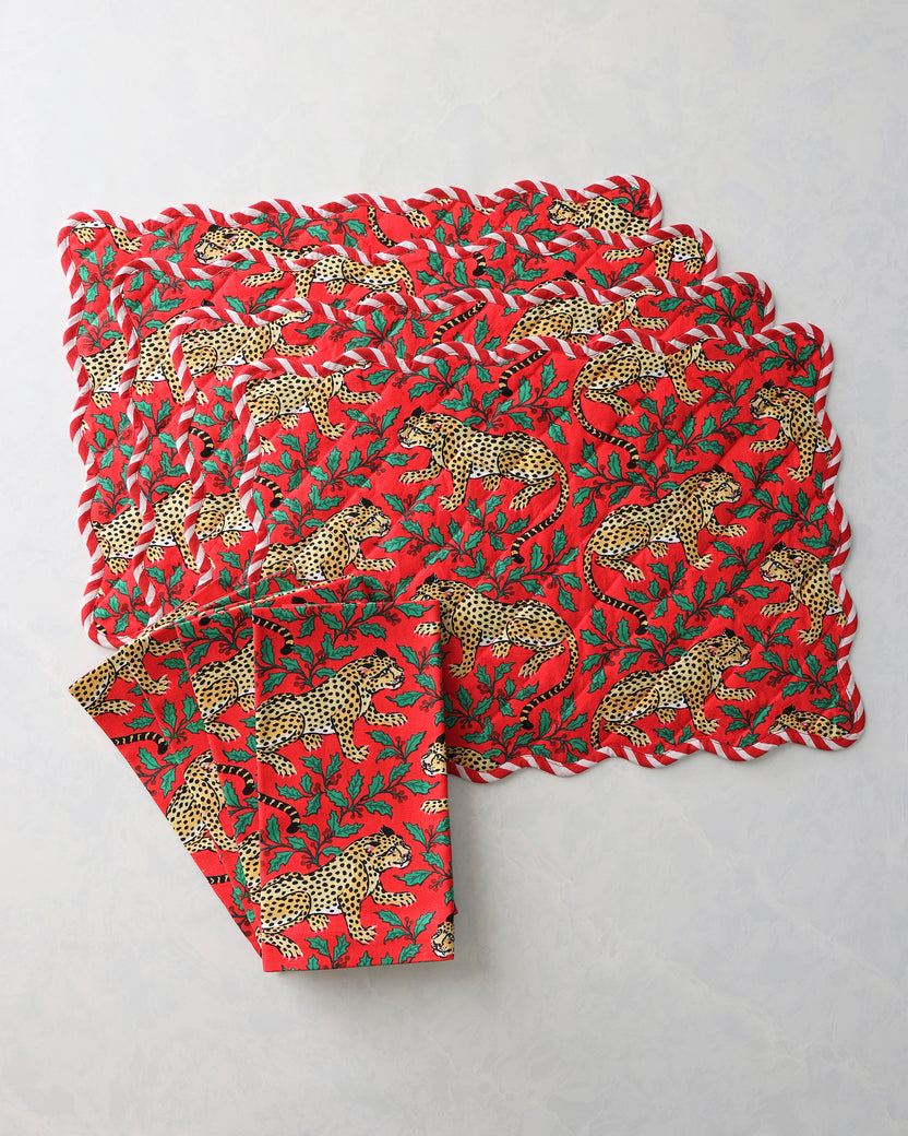 Stacked red placemats and napkins with leopard and holly print.