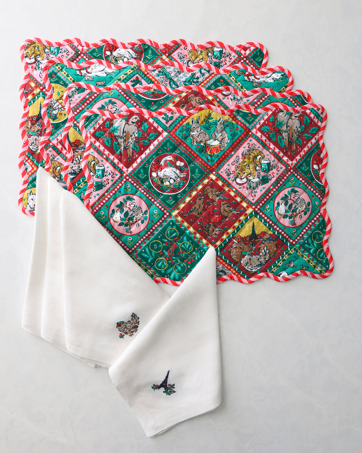 Stacked Christmas-themed placemats with oversized white napkins featuring small embroidered motifs.