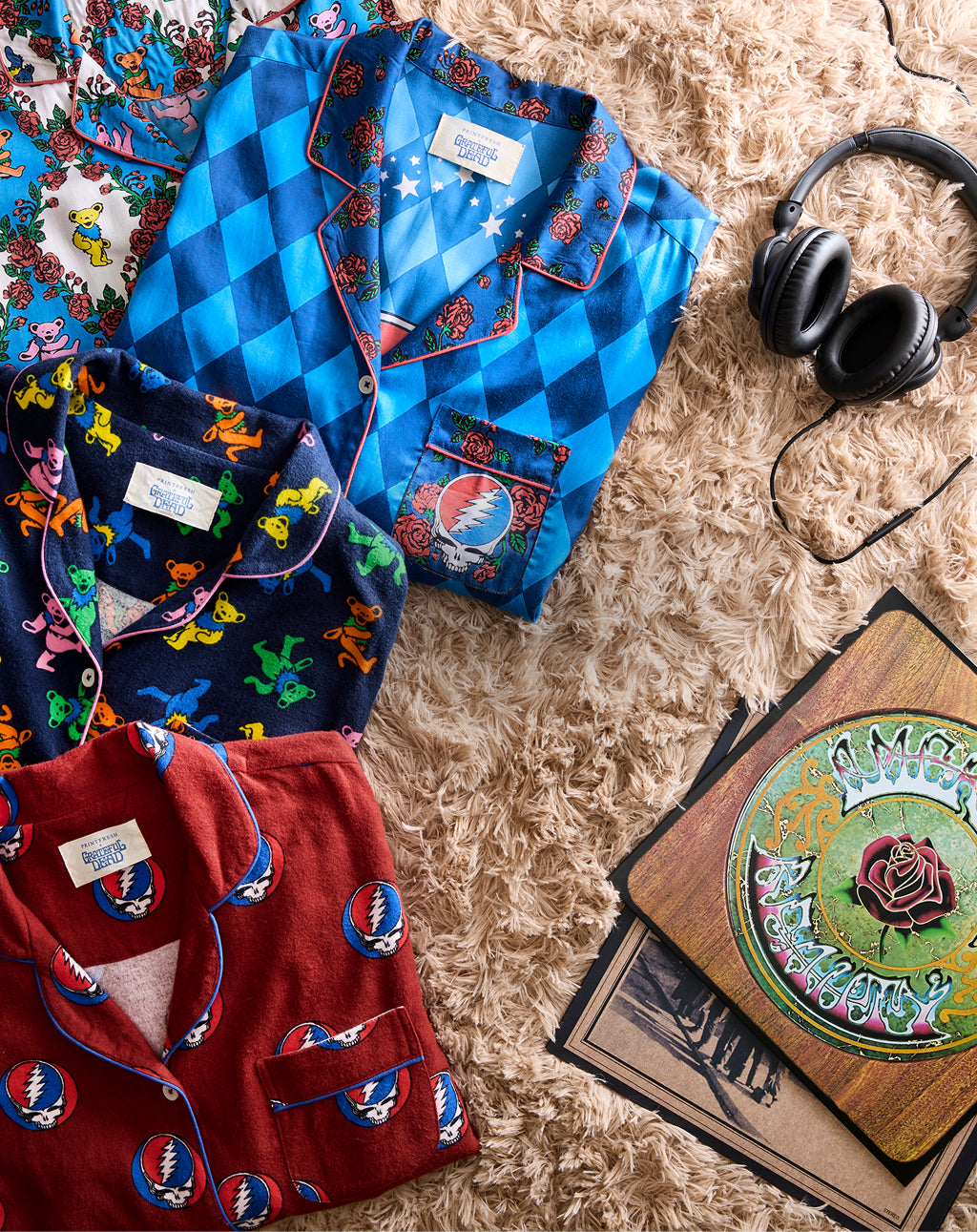 Flat lay of several colorful patterned garments arranged on a shaggy rug beside black headphones and record covers.