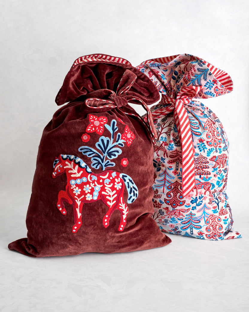 Two tied gift sacks, including a burgundy sack with an embroidered horse and a light patterned sack with red and blue motifs.
