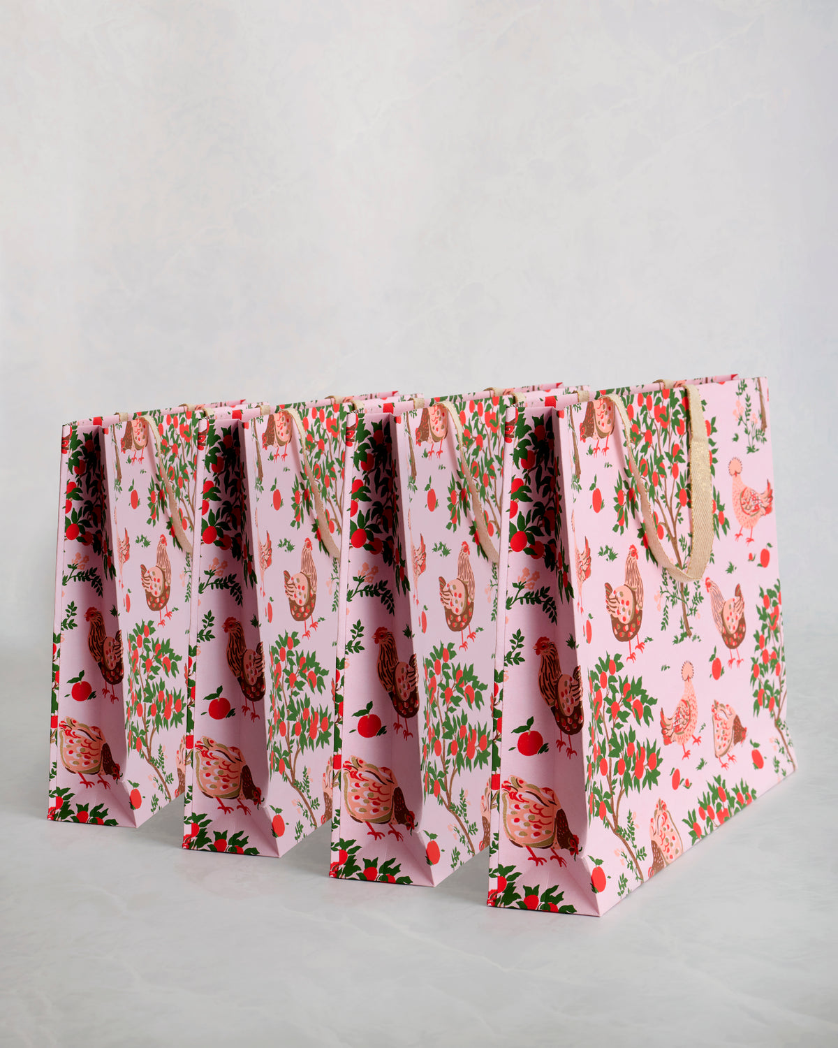 Set of four pink paper gift bags with chicken illustrations, foliage, and matching handles.