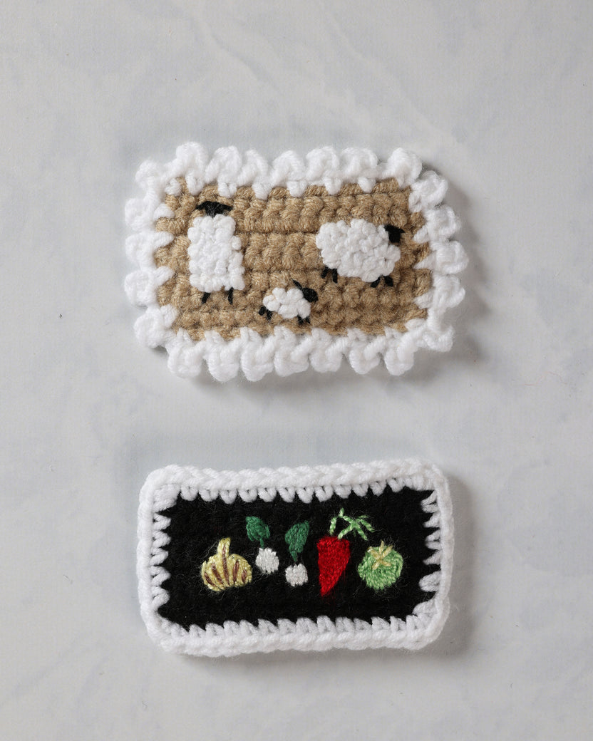 Two crochet snap hair clips, one with a sheep design and one with embroidered farm vegetables.