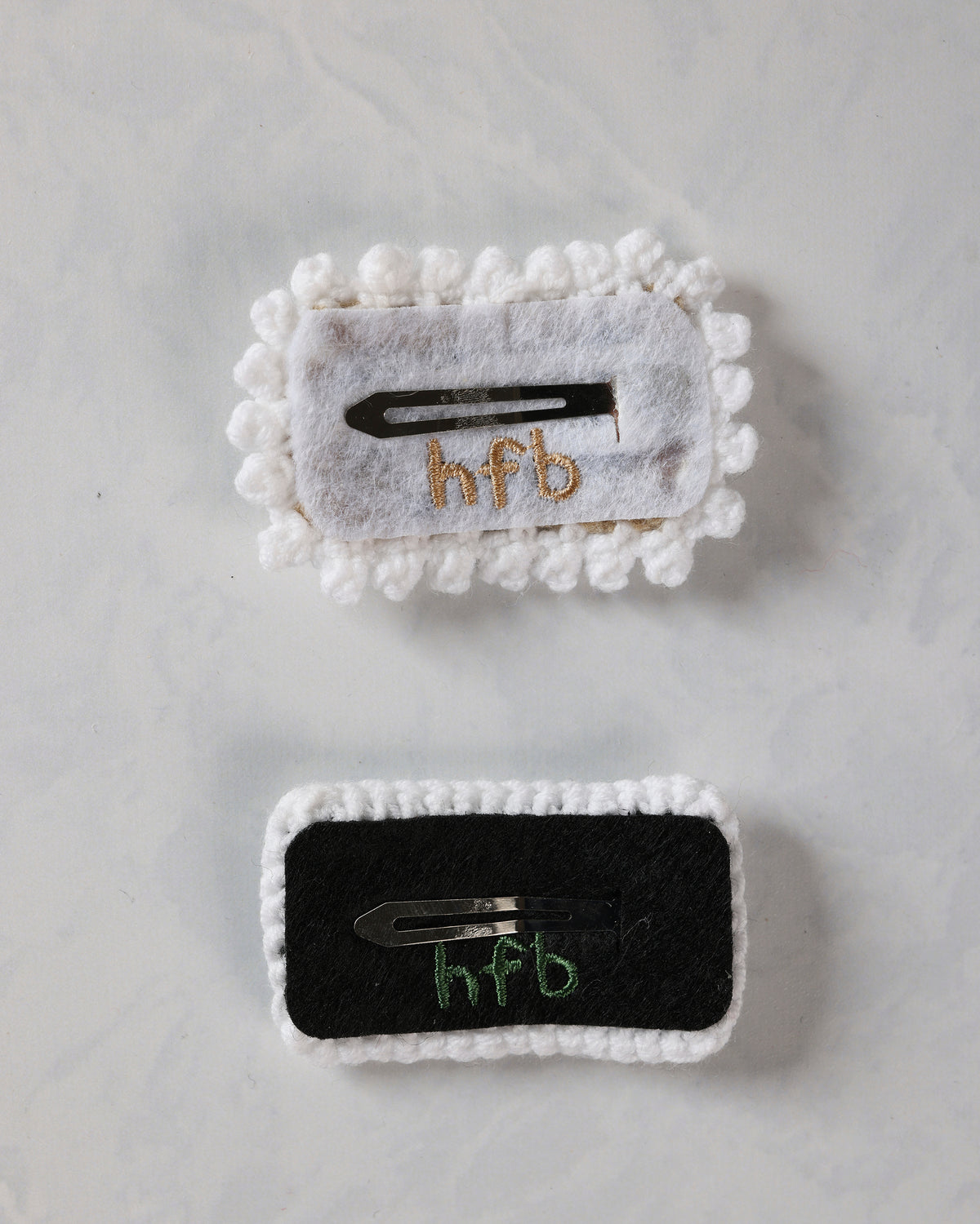 Backs of two crochet snap hair clips showing their metal clips and fabric backing.