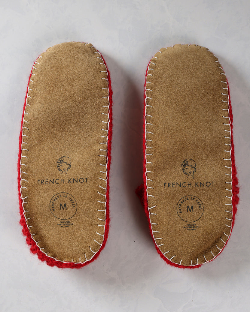 Bottom view of the pair of slippers showing tan leather soles with stitched edges and French Knot markings.