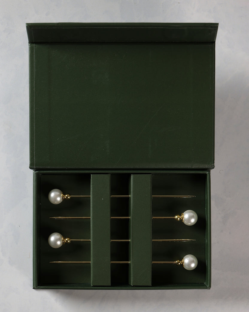 Open dark green presentation box containing four pearl-topped cocktail picks.