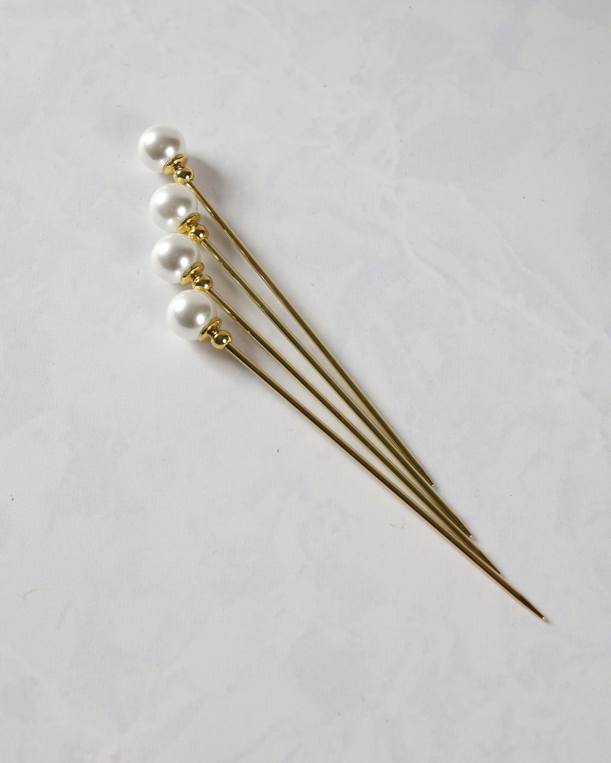 Four gold cocktail picks with faux pearl tops arranged diagonally.