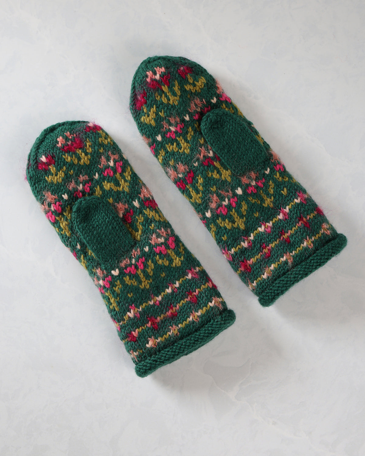 Pair of patterned green knitted mittens shown at an angle with thumb openings and ribbed cuffs.
