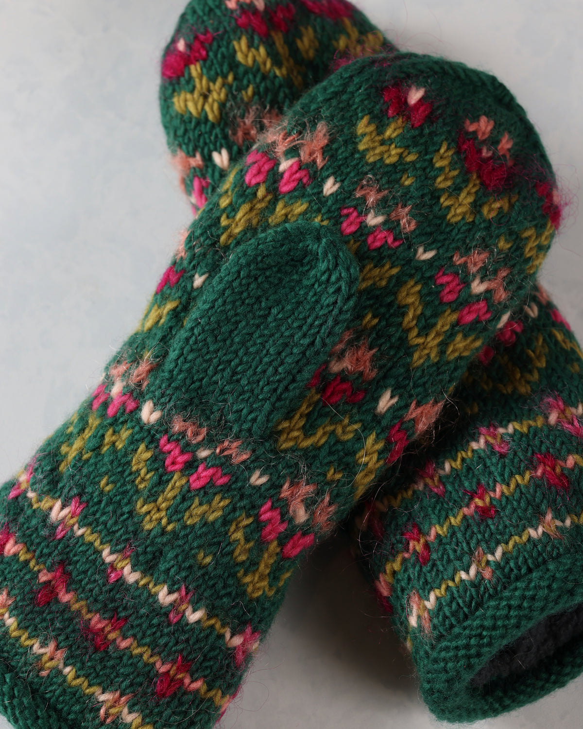 Close-up of two green knitted mittens showing the floral pattern, thumb openings, and textured stitching.
