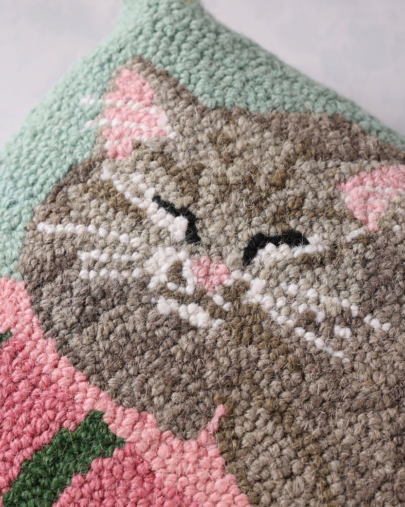 Close-up of the hooked pillow showing the sleeping cat's face, pink ears, and textured stitching above the books.