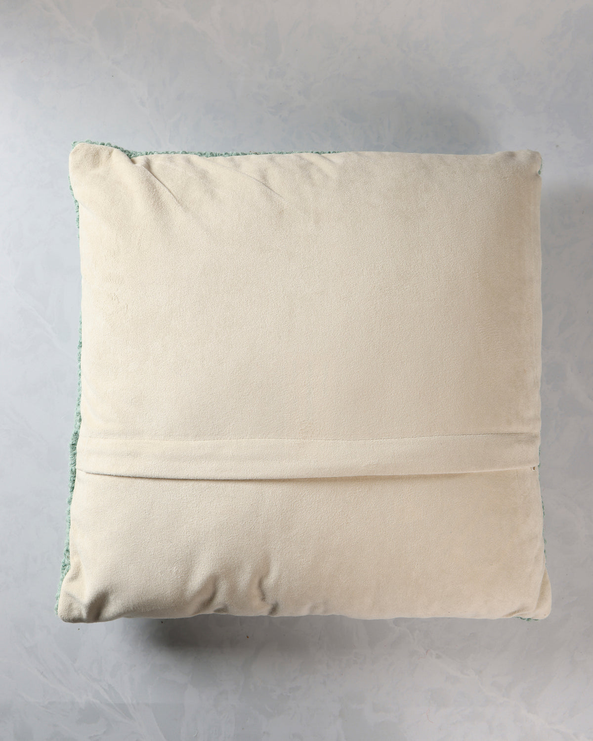 Back of the square pillow showing a plain cream-colored fabric backing with a horizontal closure seam.
