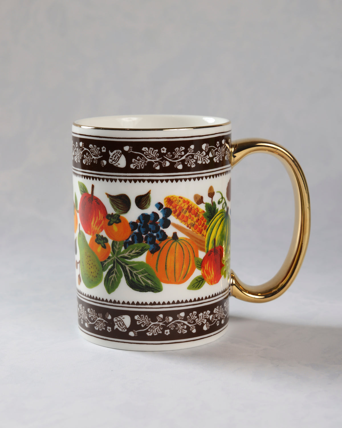 Harvest porcelain mug with a gold handle and rim, decorated with pumpkins, fruit, corn, and leaves.