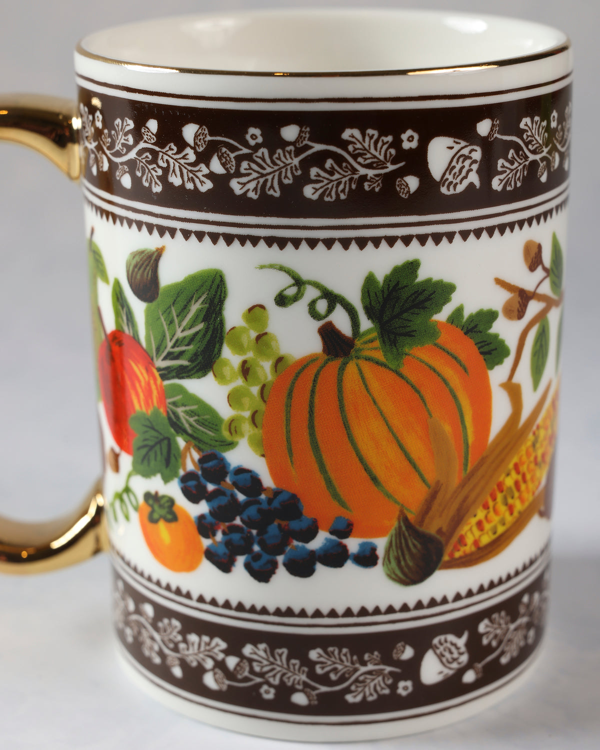 Close view of the harvest mug showing an orange pumpkin, grapes, berries, corn, and brown botanical borders.