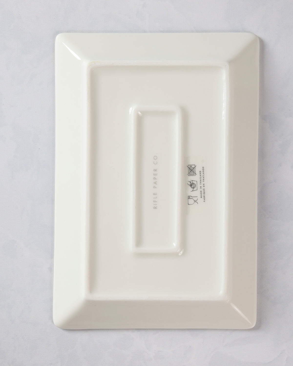 Back of a rectangular porcelain catchall tray with raised rectangular sections and printed Rifle Paper Co. markings.