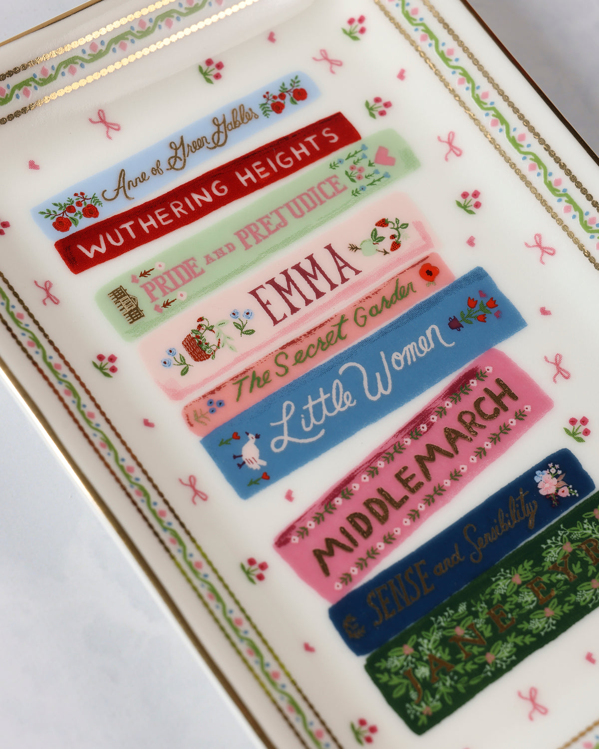 Close angled view of the catchall tray showing illustrated book spines and floral border details.