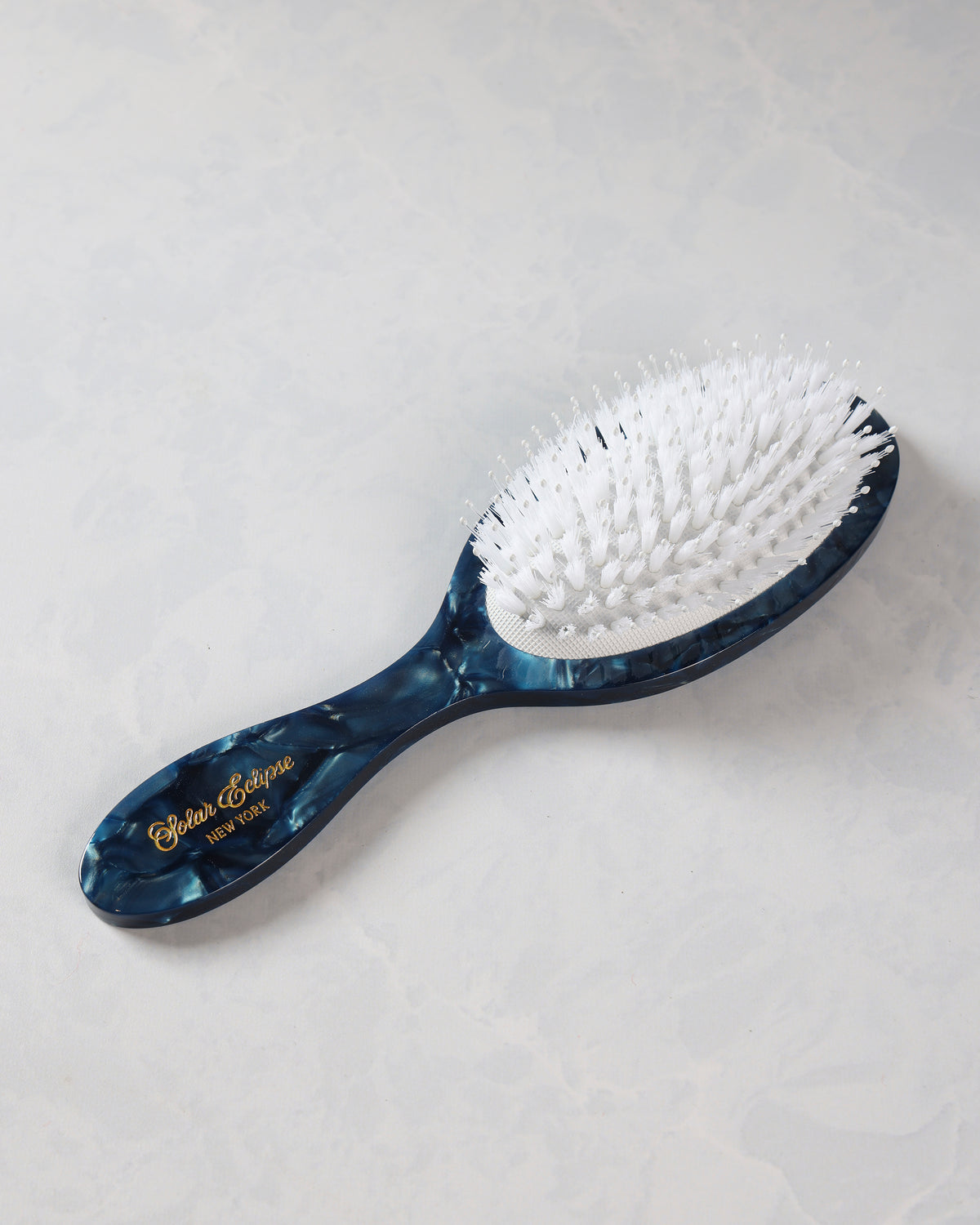 Full view of a dark blue patterned hair brush with white bristles and a curved handle.