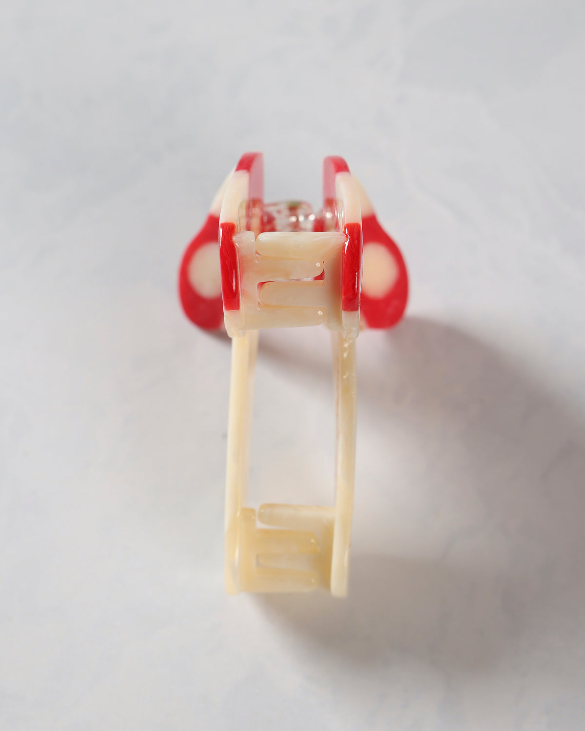 Red-and-cream mushroom-pattern claw hair clip shown from the front with its open jaws visible.