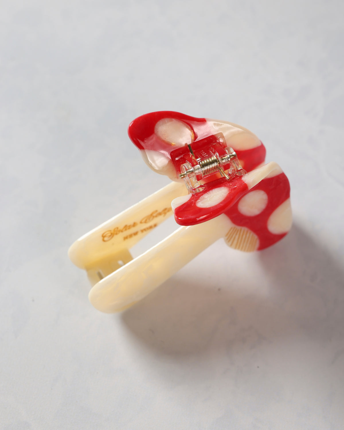 Open red-and-cream mushroom-pattern claw hair clip showing its metal hinge and teeth.