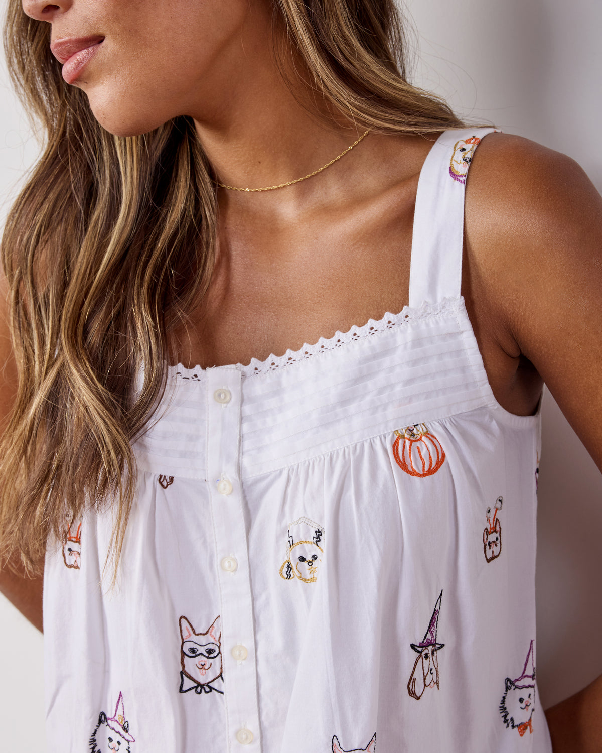 Close-up of the nightgown bodice showing the scalloped trim, shoulder strap, buttons, and embroidered dog and pumpkin motifs.
