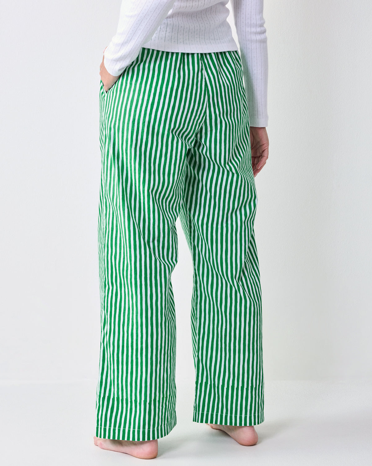 Back view of green-and-white vertically striped pajama pants with wide legs and side pockets.