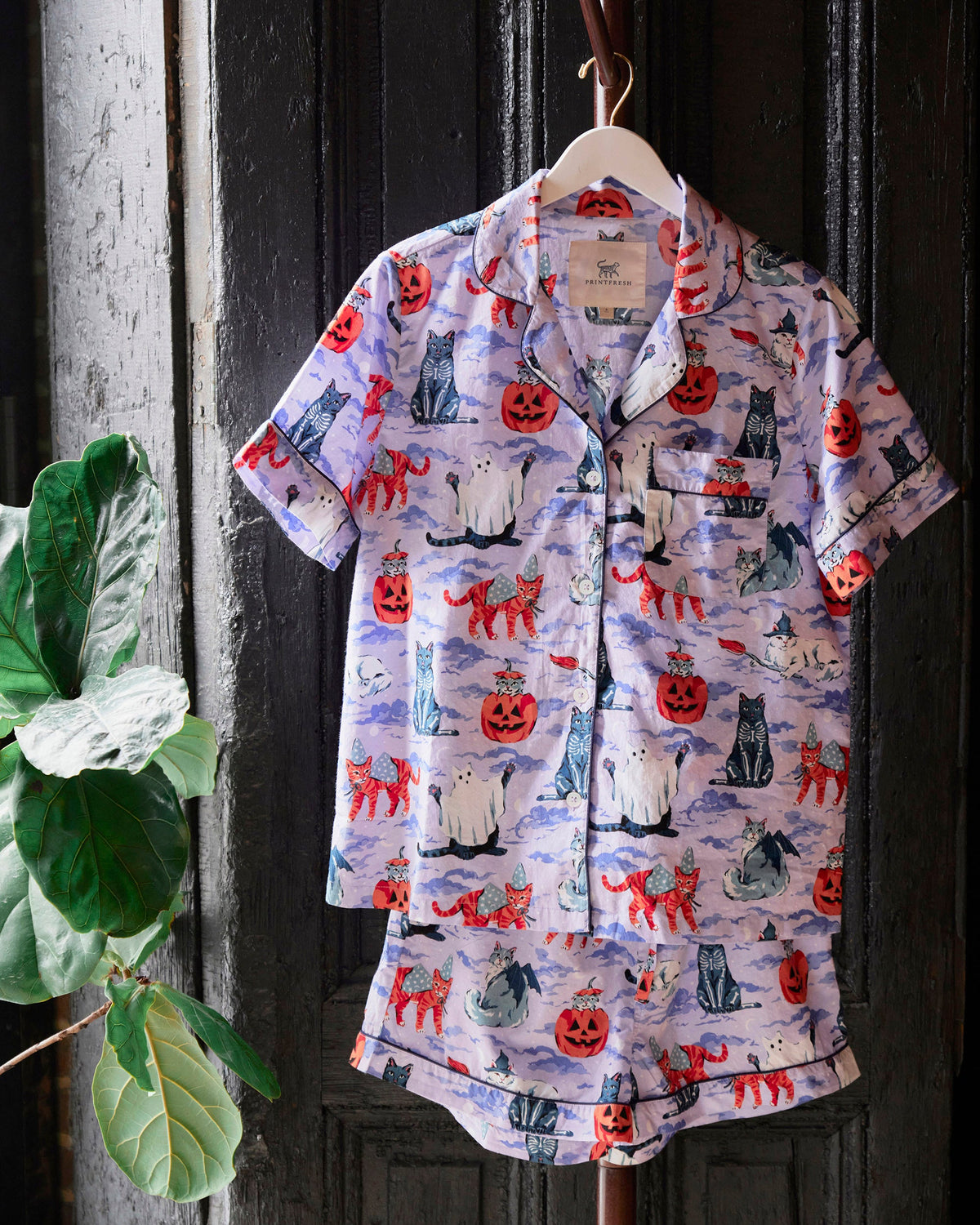Lavender Halloween House Cats short pajama set hanging on a hanger, showing the button-down top and matching shorts.