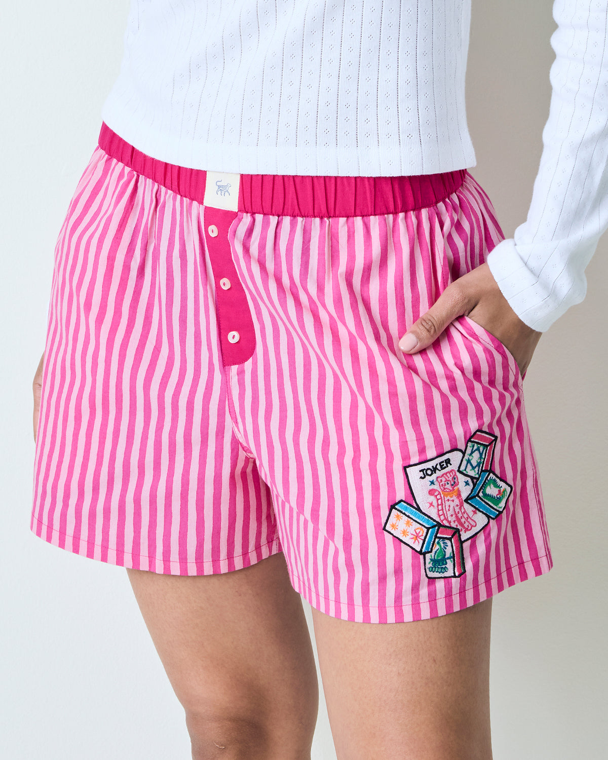 Close-up of the hot pink striped Eloise boxers showing the elastic waistband, button fly, pocket, and embroidered patch.