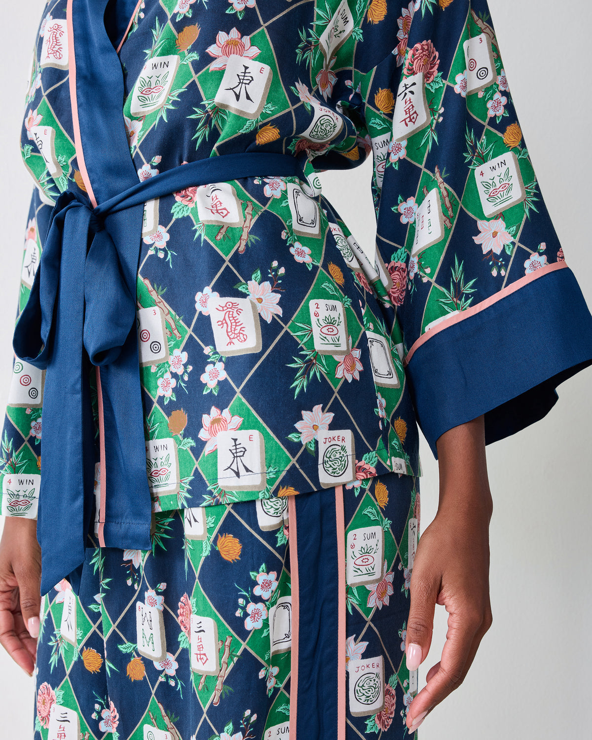 Close-up of the Mahj Garden Eco Satin Wrap Set in Wintergreen, showing the tied wrap front, blue cuff, pink trim, and floral mahjong-tile print.