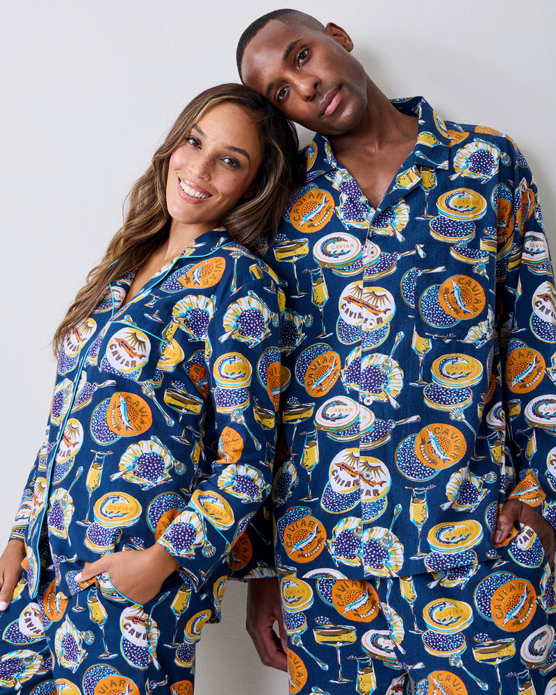 Two people pose together wearing matching navy pajamas with caviar-themed prints.