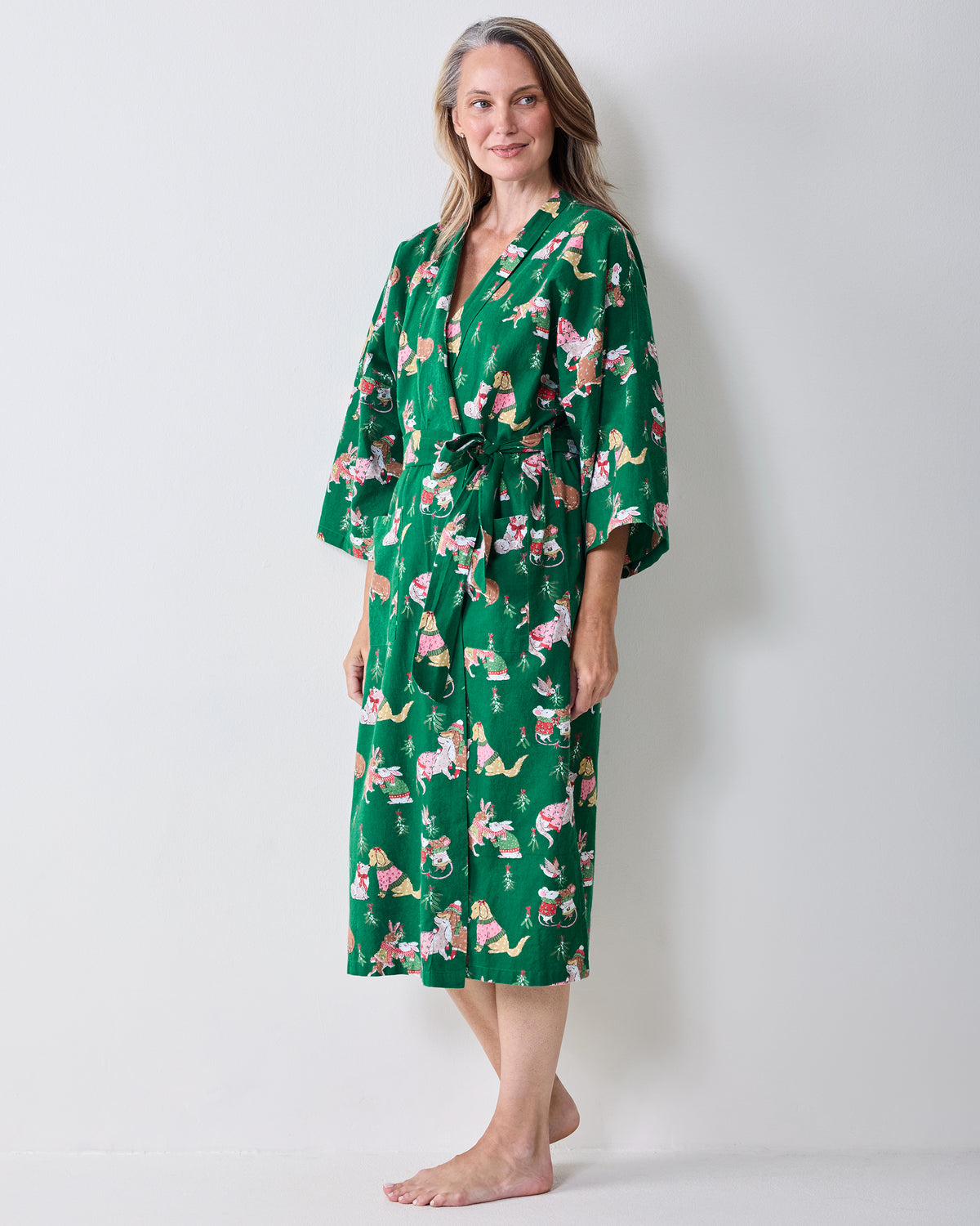 Side view of a person wearing the green Mistletoe Kiss flannel long robe with a holiday critter print and matching waist belt.