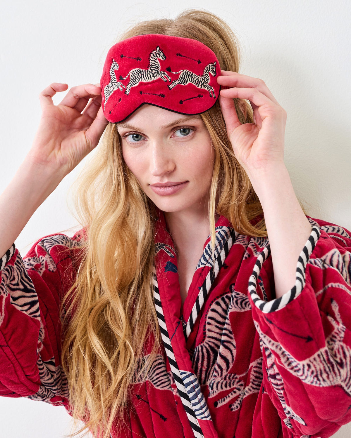 Person wearing a red embroidered zebra-print eye mask over the eyes, with a matching patterned robe visible.