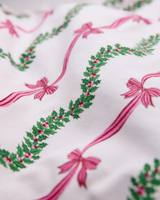 Close-up of a white printed surface with green holly garlands and pink ribbon bows.