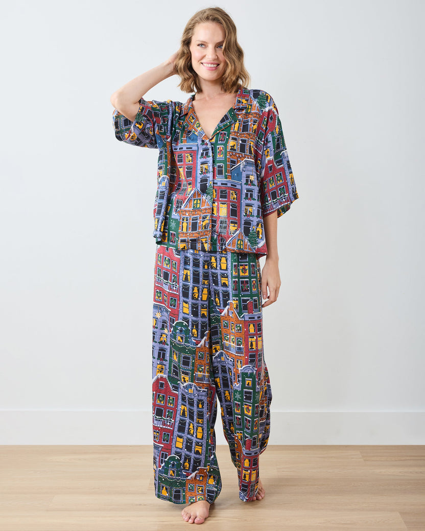 Full-length front view of a person wearing a matching short-sleeve pajama top and wide-leg pants with a colorful city-building print.