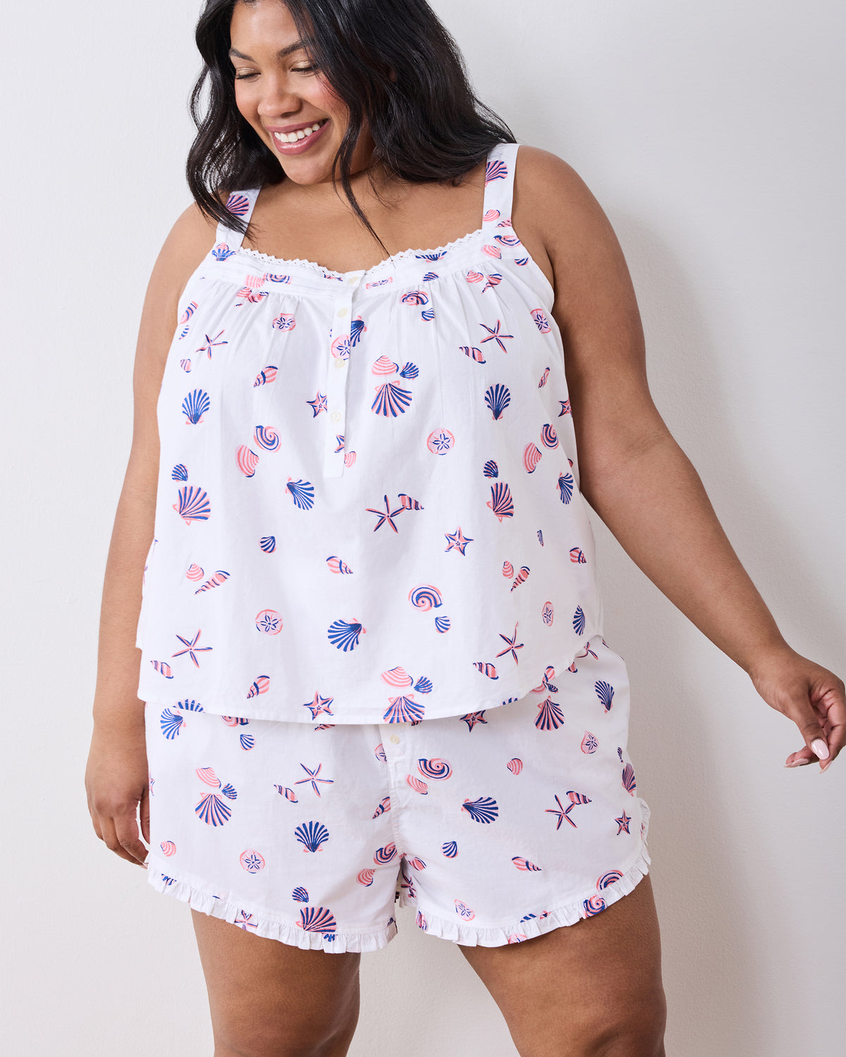 Front view of the white sleeveless pajama top and shorts with pink-and-blue shell print and ruffled trim