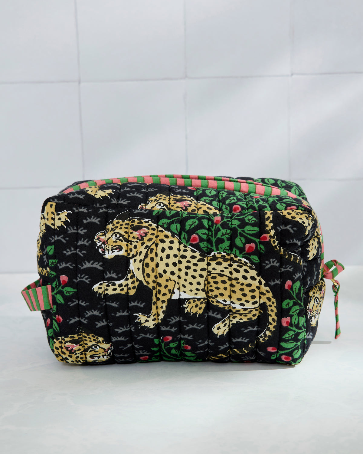 Quilted Bagheera pouch in black with leopard, leaf, and berry print, shown from the front with a striped trim and side ties.