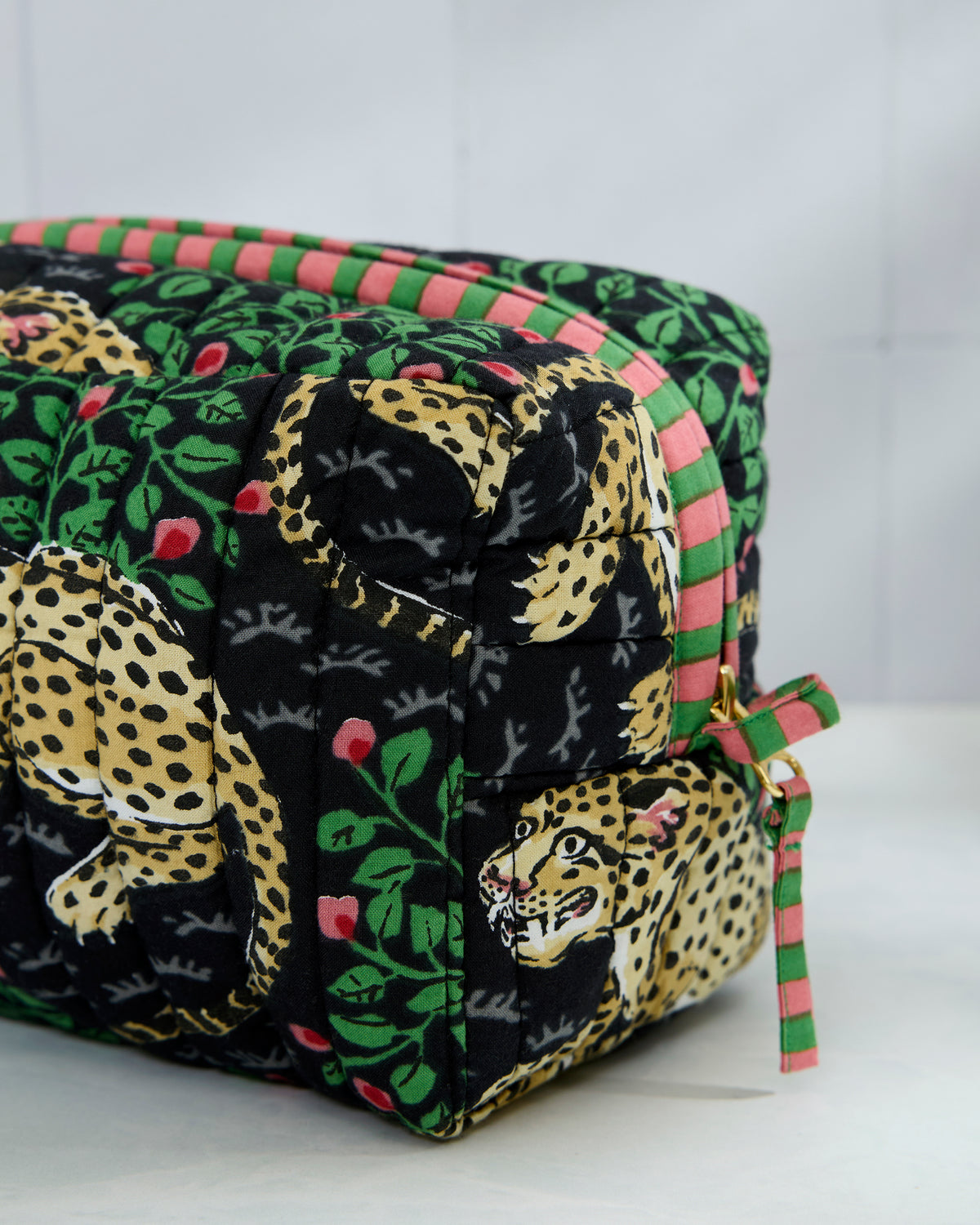 Close-up of the quilted Bagheera pouch corner, showing leopard and leaf print, striped trim, and a side tie.