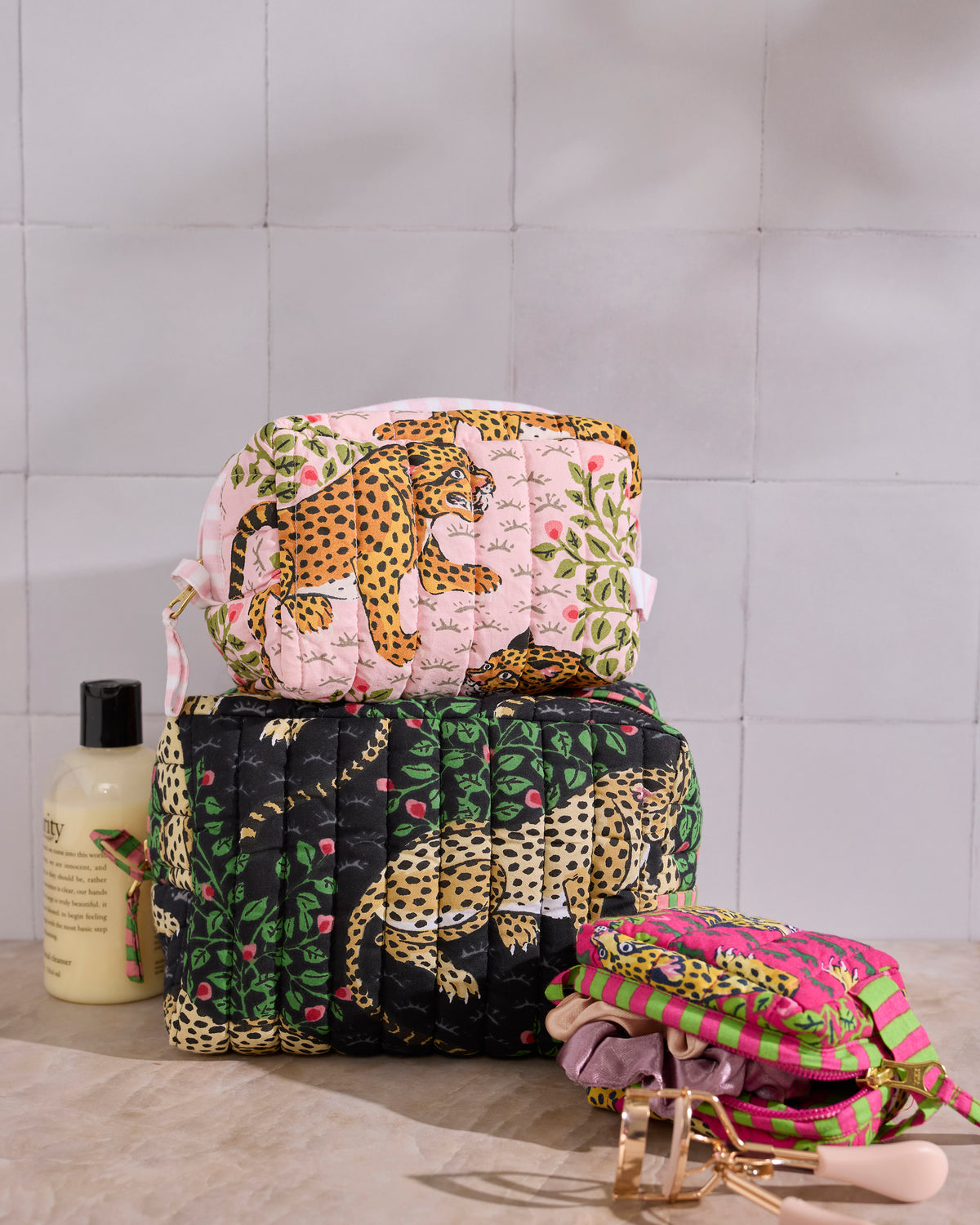 Three quilted pouches in pink and black Bagheera leopard prints, stacked beside toiletries.