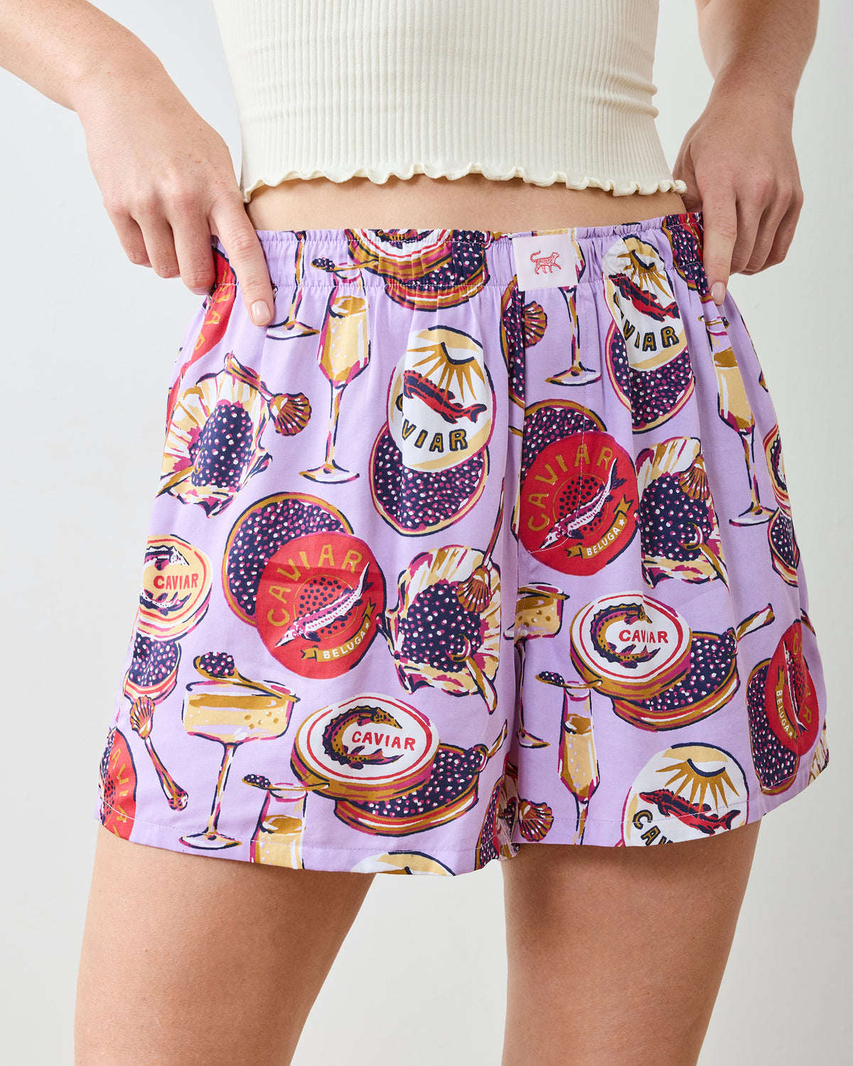 Close-up front view of lavender boyfriend boxer shorts with champagne flute and caviar-themed print, showing the waistband and front fly.