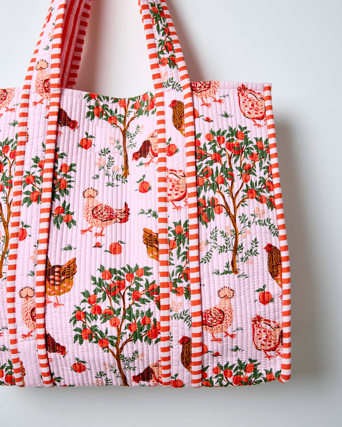 Close-up of the quilted tote bag showing its light pink farmyard print, vertical quilting, and striped trim.