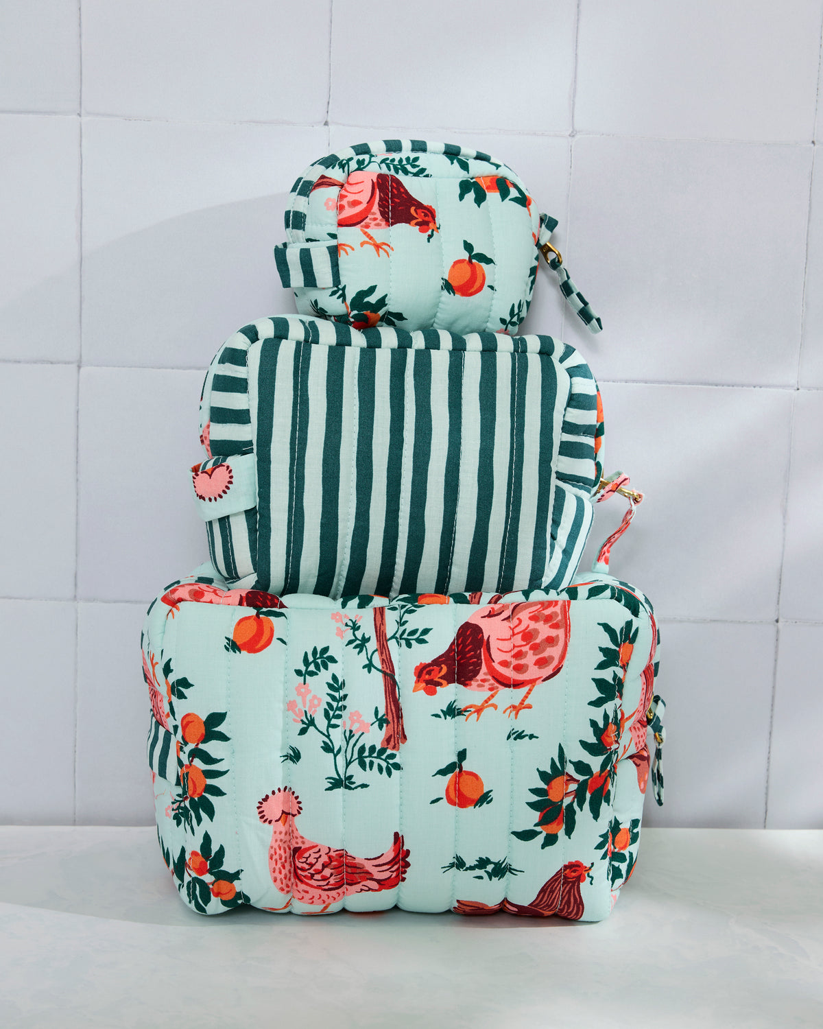 Three quilted pouches stacked by size, with a light blue farmyard print on the largest and smallest pouches and vertical stripes on the middle pouch.