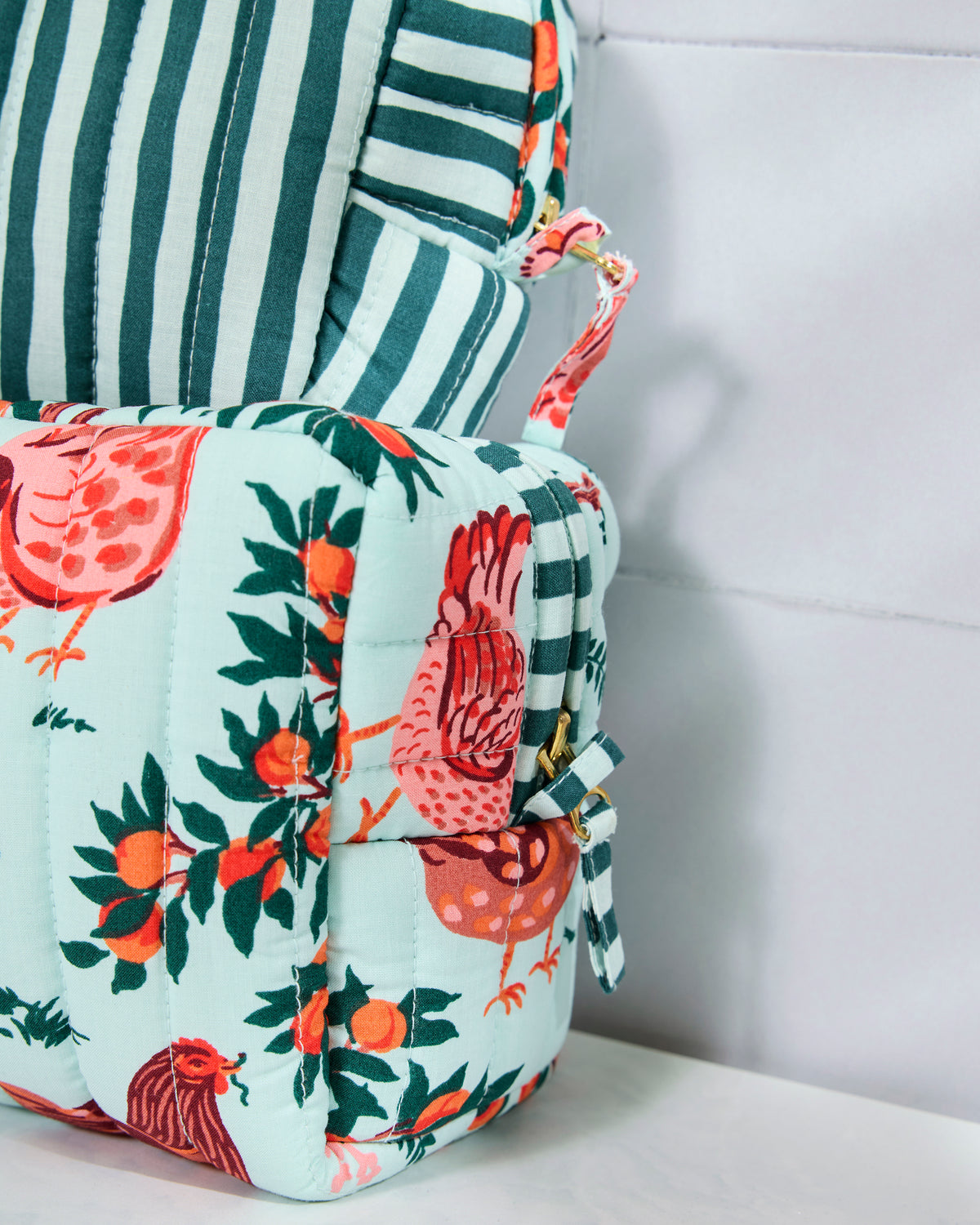 Close-up of the quilted pouch set showing the light blue farmyard print, striped pouch, zippers, and side hardware.