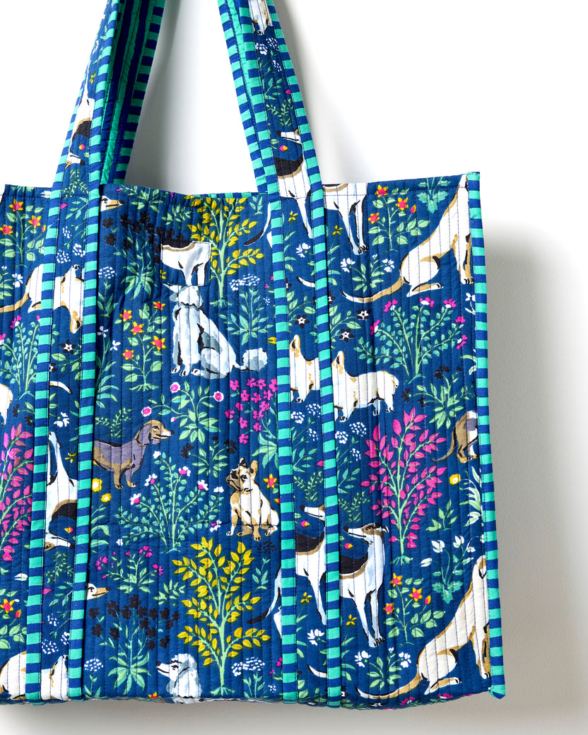 Close view of the indigo quilted traveler tote showing dog-and-flower print panels, striped handles, and a front pocket.
