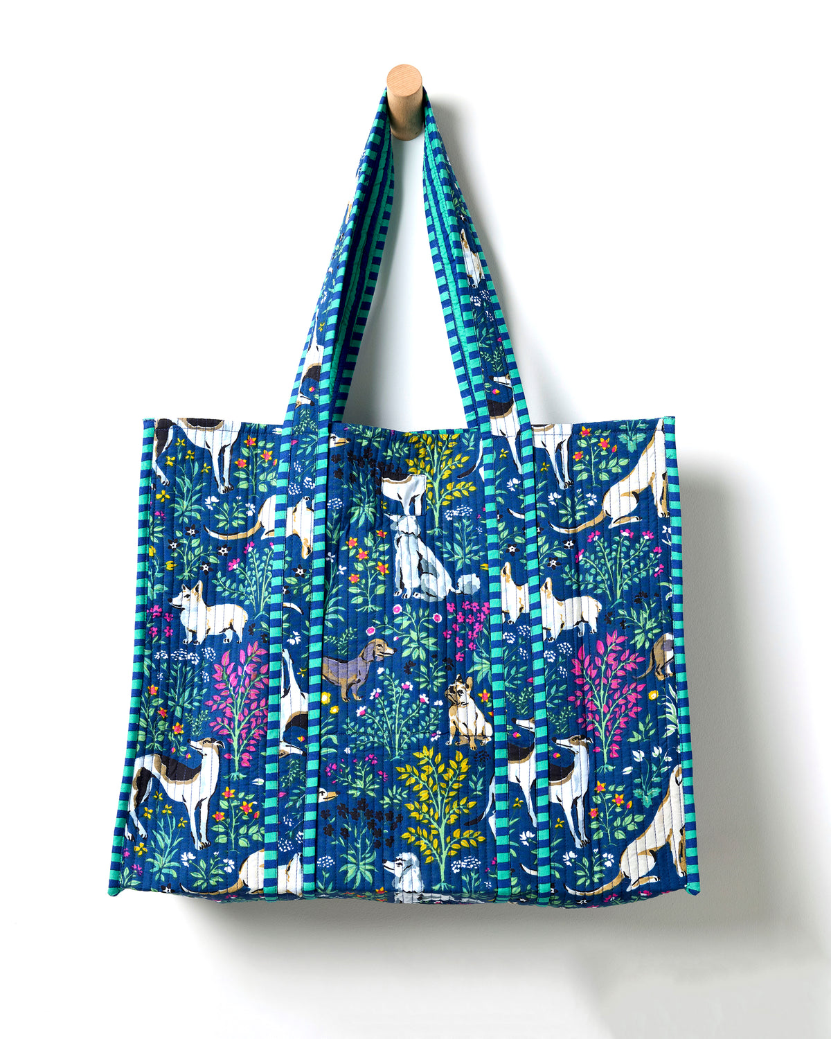 Full view of an indigo quilted traveler tote with dog-and-flower print, striped handles, and a structured rectangular shape.