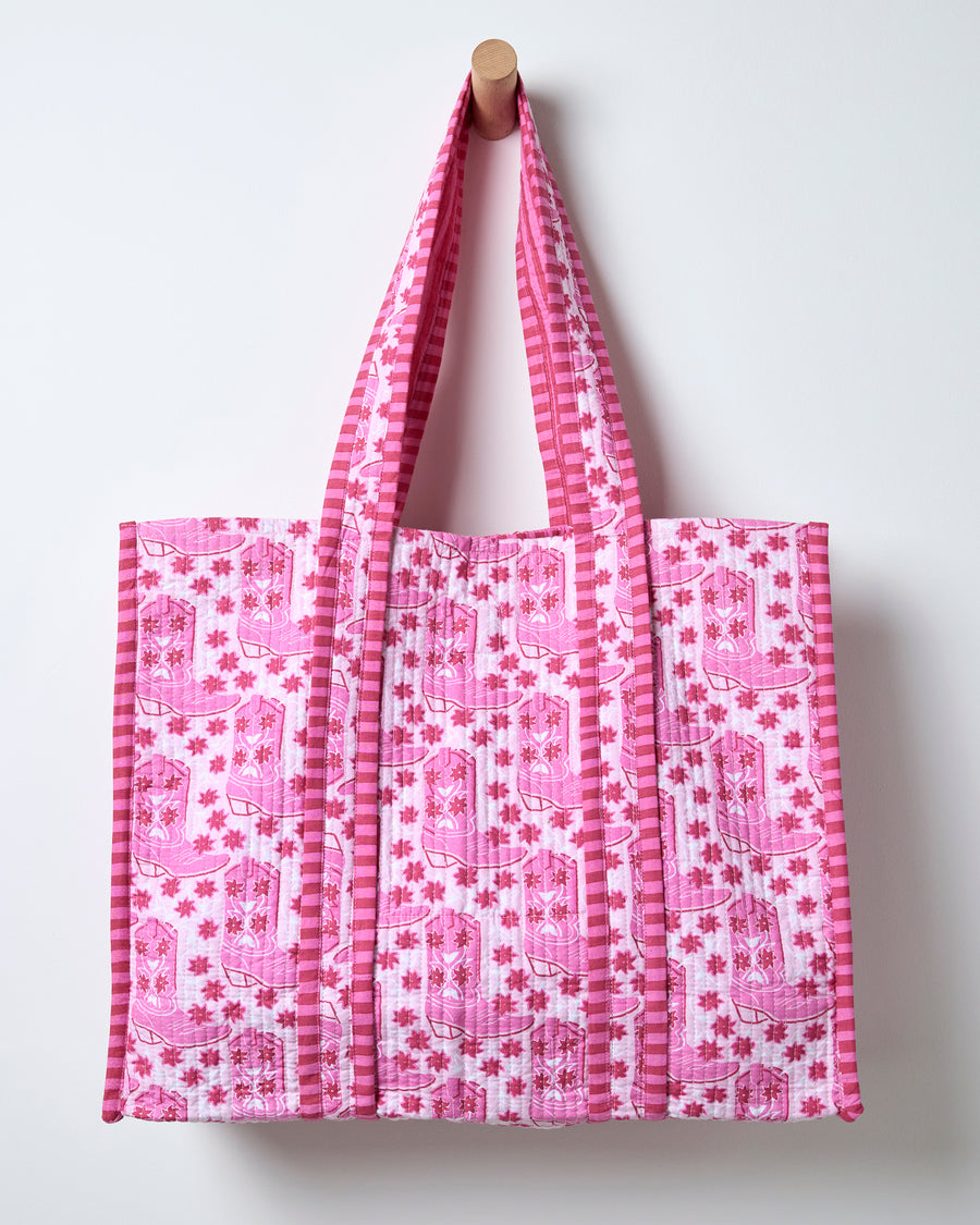 Full view of a pink quilted traveler tote with repeated western boot print and matching striped handles and trim.